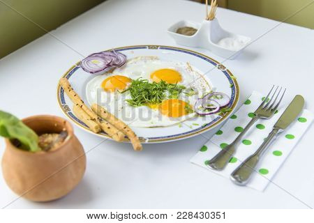 Three Fried Eggs On A Ceramic Plate, Some Parsley, Breadsticks And Onions With Orange Salad Dressing