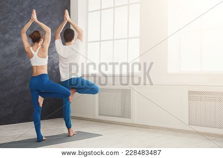 Man And Woman Training Yoga In Tree Pose. Young Couple Making Relaxing Exercise, Copy Space. Partner