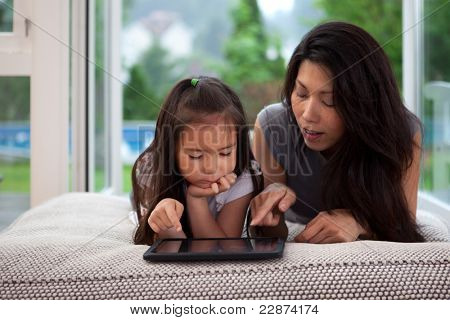Madre e figlia posa sul divano giocando con una tavoletta digitale