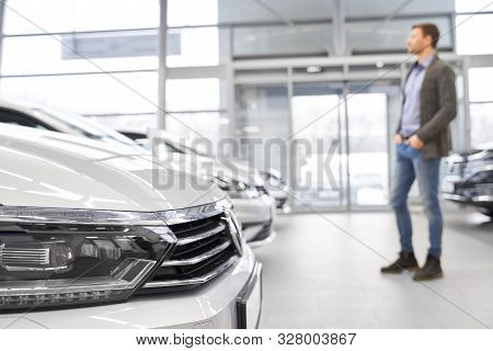 Selective Focus Of Headlights Of Big White Car In Auto Salon. Young Male Customer Looking At New Car