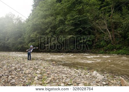 Boy near the river is dropping stones in the water. Boy have fun