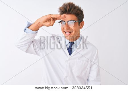 Young handsome sciencist man wearing glasses and coat over isolated white background very happy and smiling looking far away with hand over head. Searching concept.