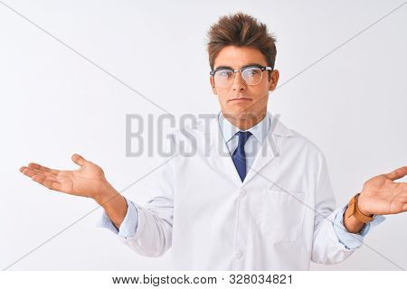 Young handsome sciencist man wearing glasses and coat over isolated white background clueless and confused expression with arms and hands raised. Doubt concept.