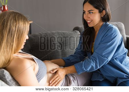 Midwife Examining Expectant Mother At Home. Young Woman Touching Belly Of Pregnant Patient Lying On 