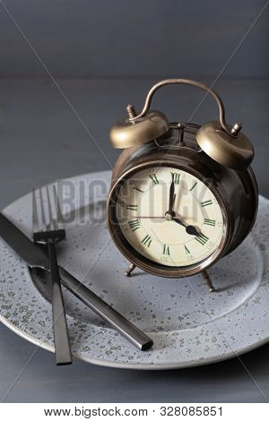 concept of intermittent fasting, ketogenic diet, weight loss. fork and knife crossed and alarmclock on plate