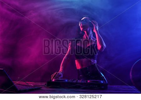 Young Sexy Woman Dj In Bra And Sunglasses Playing Music. Headphones And Dj Mixer On Table. Colorful 