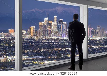 Businessman Wearing A Suit Looking At The Buildings Of Downtown Los Angeles From An Office Window.  