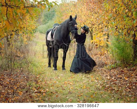 Horsewoman Girl In A Black Dress Leads A Black Horse