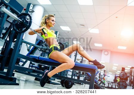 Gorgeous Blonde Woman Posing On Sports Equipment At A Gym Looking Straight In Front Of Her. She Wear