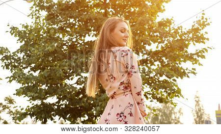 Nice Young Woman With Loose Fair Hair In Pink Dress Smiles And Poses For Camera Against Bright Sun C