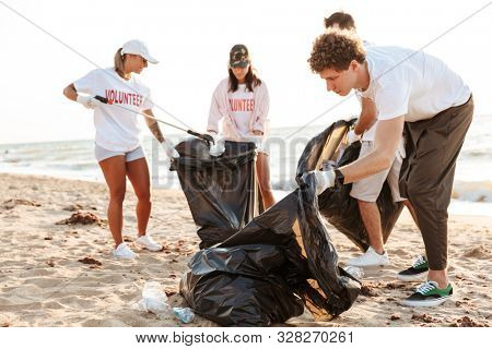Photo of concentarted volunteers workers cleaning beach from plastic with trash bags at seaside