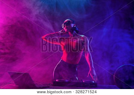 Young Sexy Woman Dj Playing Music. Headphones And Dj Mixer On Table. Colorful Smoke On Background