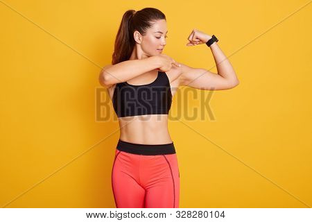 Horizontal Shot Of Beautiful Brunette Young Woman Dresses Black Top And Leggins, Pointing At Her Bic