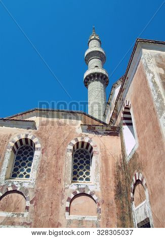 The Suleiman Mosque In Rhodes Old Town With Tall Minaret Against A Blue Sunlit Sky