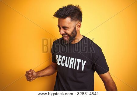 Arab indian hispanic safeguard man wearing security uniform over isolated yellow background very happy and excited doing winner gesture with arms raised, smiling and screaming for success. Celebratio