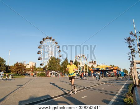 Novosibirsk, Russia - 08.25.2019: Running Man Against Two Large Ferris Wheels In The Park On Mikhail