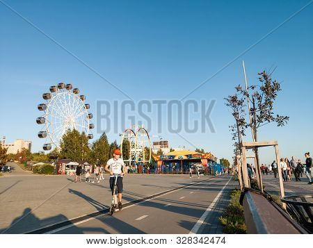 Novosibirsk, Russia - 08.25.2019: Scooters And Skaters Against Two Large Ferris Wheels In The Park O