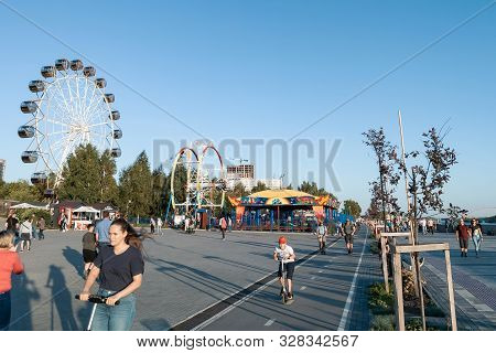 Novosibirsk, Russia - 08.25.2019: Scooters And Skaters Against Two Large Ferris Wheels In The Park O