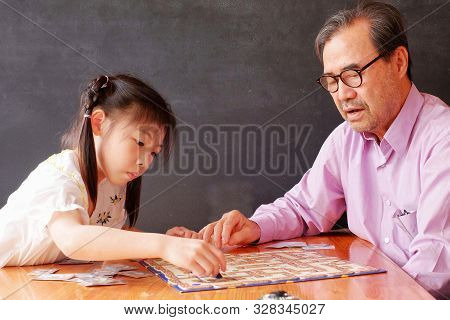 An Cute Asian Preschool Girl Learning To Play Board Games With Her Grandfather