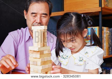 An Grandfather Is Teaching His Granddaughter To Play A Block Wood Tower Game.