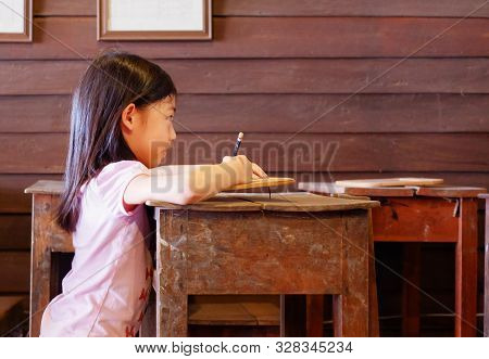 A Thai Schoolgirl Studying In Her Classroom In Rural Thailand With Old Wooden Table And Antique Ston