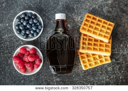 Waffles, maple sirup, blueberries and raspberries on old kitche table. Top view. Flat view.