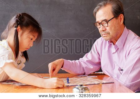 An Attractive Asian Preschool Girl Learning To Play Board Games With Her Grandfather