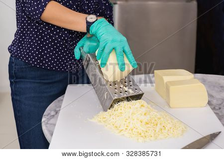 Woman With Green Gloves Grating Cheese On Kitchen Table.