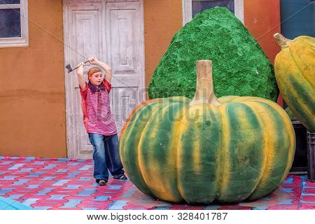 Funny Picture Of A Lilliput Toy Boy Is Cutting A Pumpkin By An Axe.