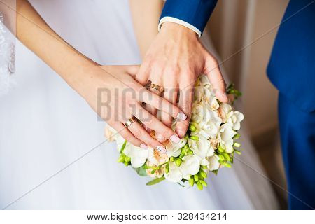 A Newly Weding Couple Place Their Hands On A Wedding Bouquet Showing Off Their Wedding Rings.