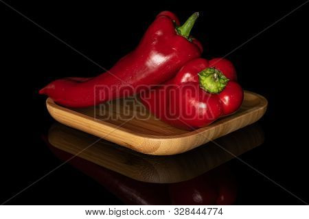 Group Of Two Whole Sweet Red Bell Pepper On Wooden Square Plate Isolated On Black Glass