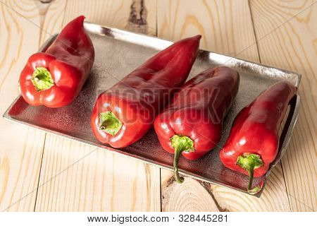 Group Of Four Whole Sweet Red Bell Pepper On Tray On Natural Wood