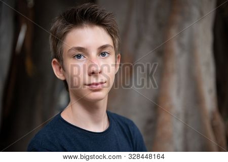 Handsome young boy at summer park. Beautiful calm smiling teen boy against nature background. Teenage lifestyle.
