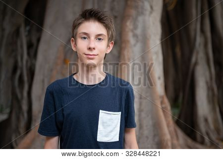 Handsome young boy at summer park. Beautiful calm smiling teen boy against nature background. Teenage lifestyle.