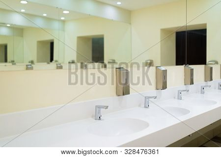 Diagonal View Of Cutting-edge Public Toilet Room With White Ceramic Basins And Soapbox.