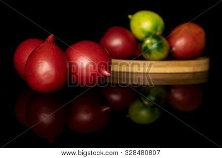 Group Of Seven Whole Fresh Tomato De Barao On Round Bamboo Coaster Isolated On Black Glass