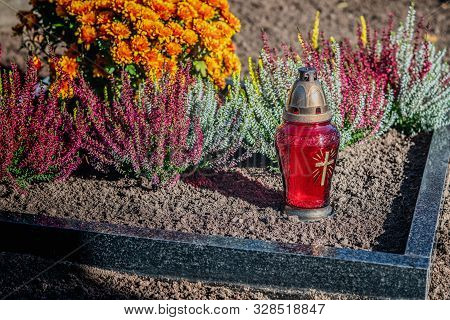 Red Lantern With Cross And Flowers On The Grave In The Cemetery. Close View.