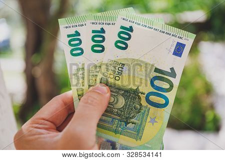 Male Hand Holding 100 Hundredth Euro Banknotes On Green Background Outdoors, Closeup