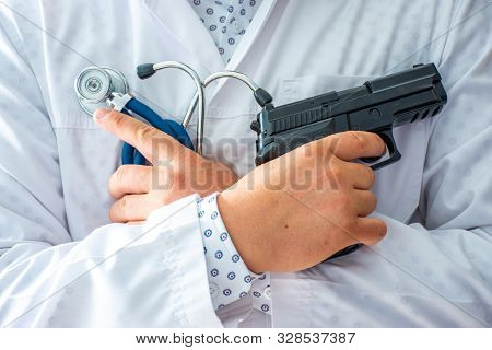 Doctor Standing And Holding Gun In One Hand And Stethoscope In Other With His Hands Crossed On His C