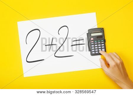Blank Paper With Task 2 Plus 2 And With A Solution On Calculator With Hand On Yellow Background. Edu