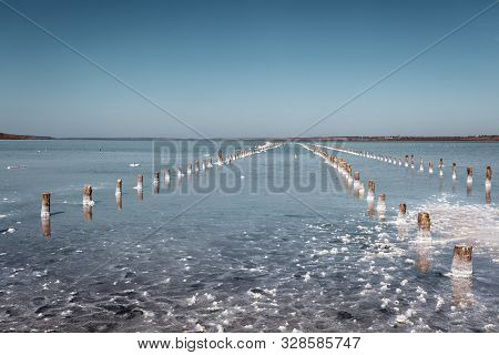 Salt Lake In The South Of Ukraine With Mud Baths. Blue Sky On A Sunny Day. Wooden Posts For Salt Min