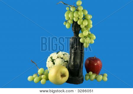 Flores, frutas e estatueta
