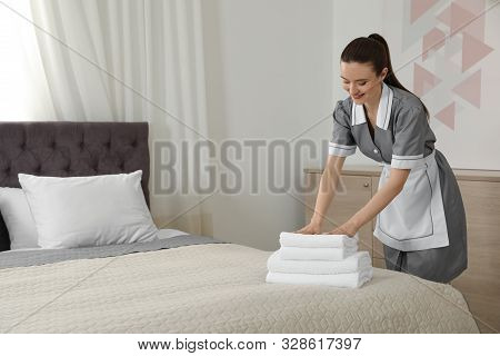 Chambermaid Putting Fresh Towels On Bed In Hotel Room. Space For Text