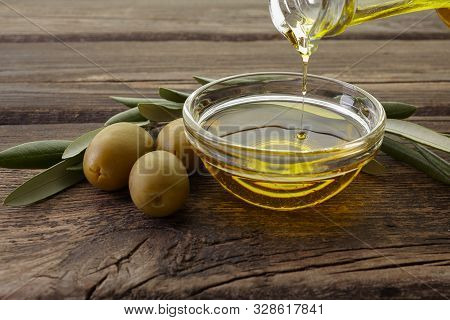 Bottle Pouring Olive Oil In A Bowl On Vintage Wooden Background