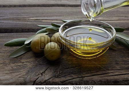 Bottle Pouring Olive Oil In A Bowl On Vintage Wooden Background