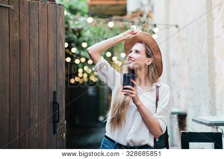 Young Attractive Woman In Casual Style Clothes Walking Along The Courtyard Of The Old City With A Cu