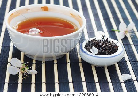 Kuppi teetä purkki teelehdet ja kirsikankukkia bamboo pöytäliinan