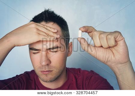 Man Holds A Pill In A Hand. Young Guy With A Headache Holds A Pill In His Hand On A Blue Medical Bac