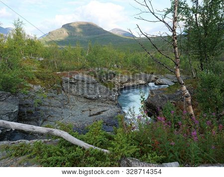 Landscape With Rapids Of Wild Blue Glaciar River Kamajakka, Rock, Birch Tree, Green Mountains And Pi