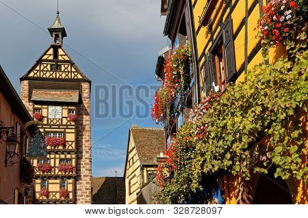 Riquewihr, France, October 13, 2019 : Tower Of The Town And Flowered Balcony. Popular Tourist Attrac